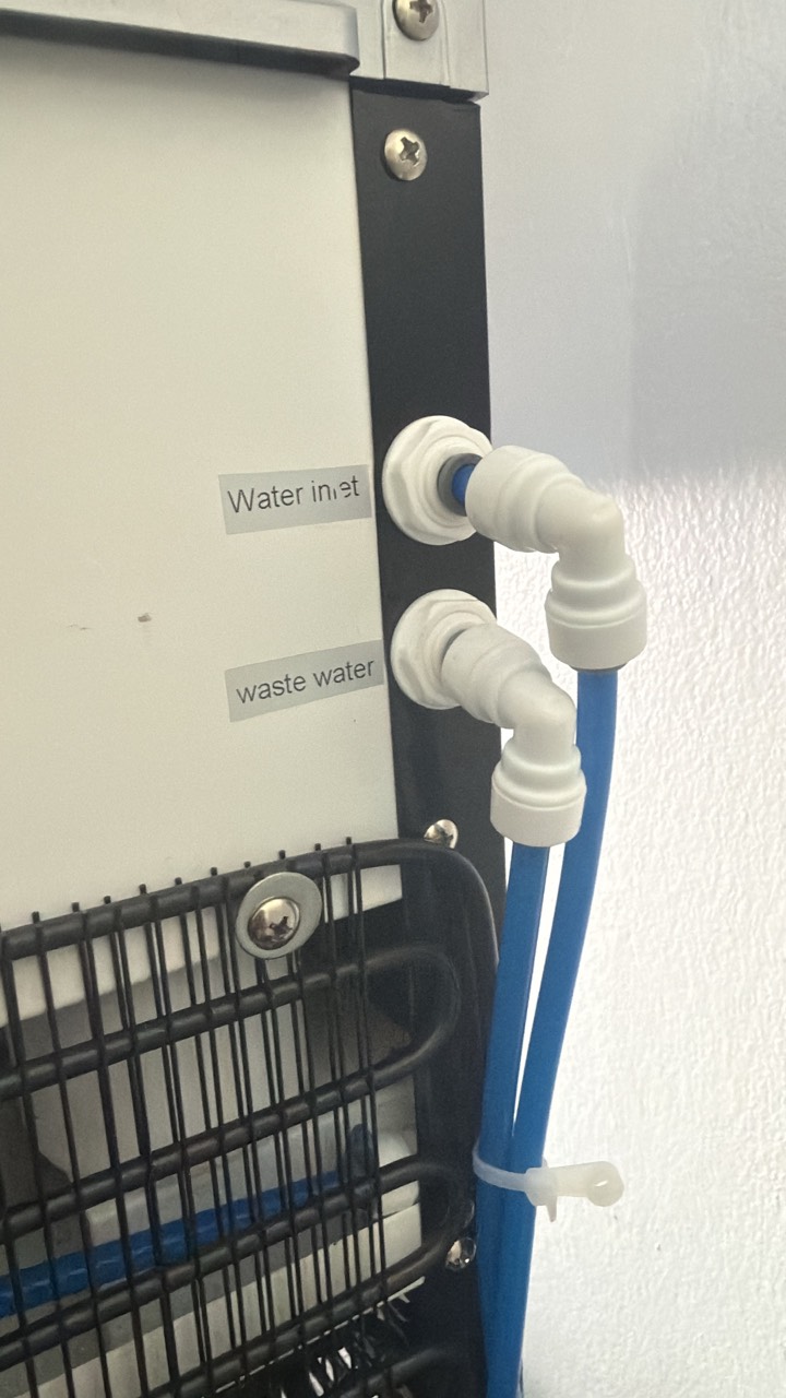 Back of the unit: water inlet and waste-water ports with blue tubing